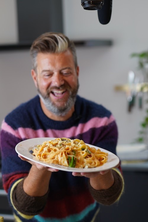 Dom smiling as he serves a plate of pasta